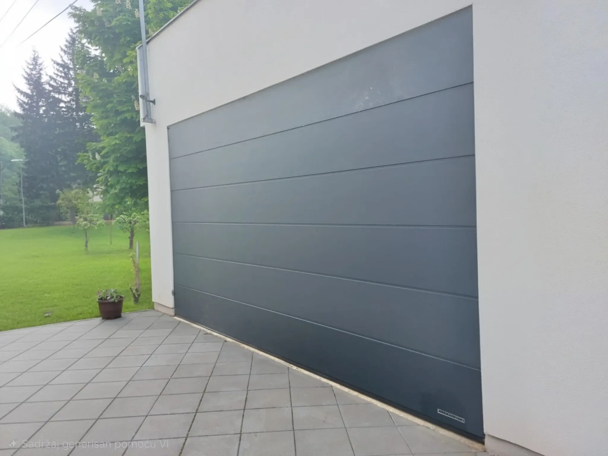 Široka segmentna garažna vrata u antracit boji sa horizontalnim rebrima na beloj fasadi